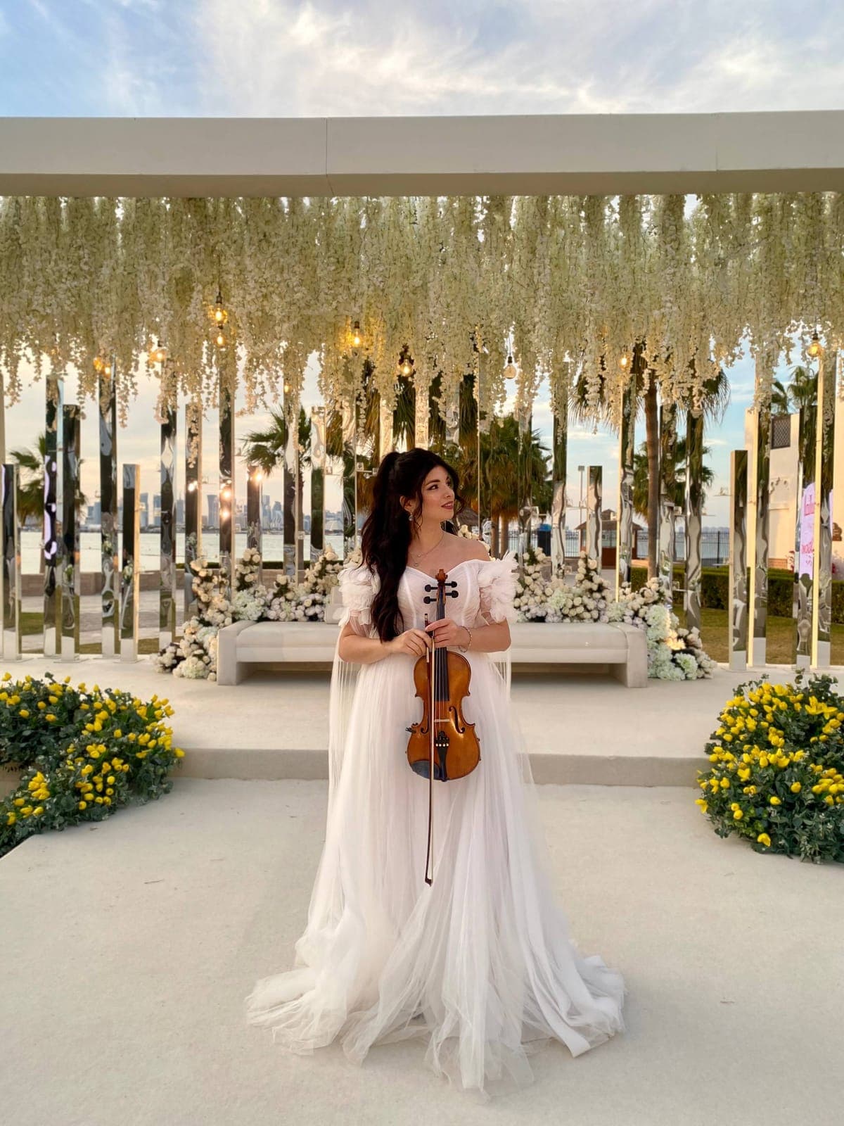 Inna Andrusenko cântă la vioară la o nuntă, în rochie albă, sub o arcadă de flori